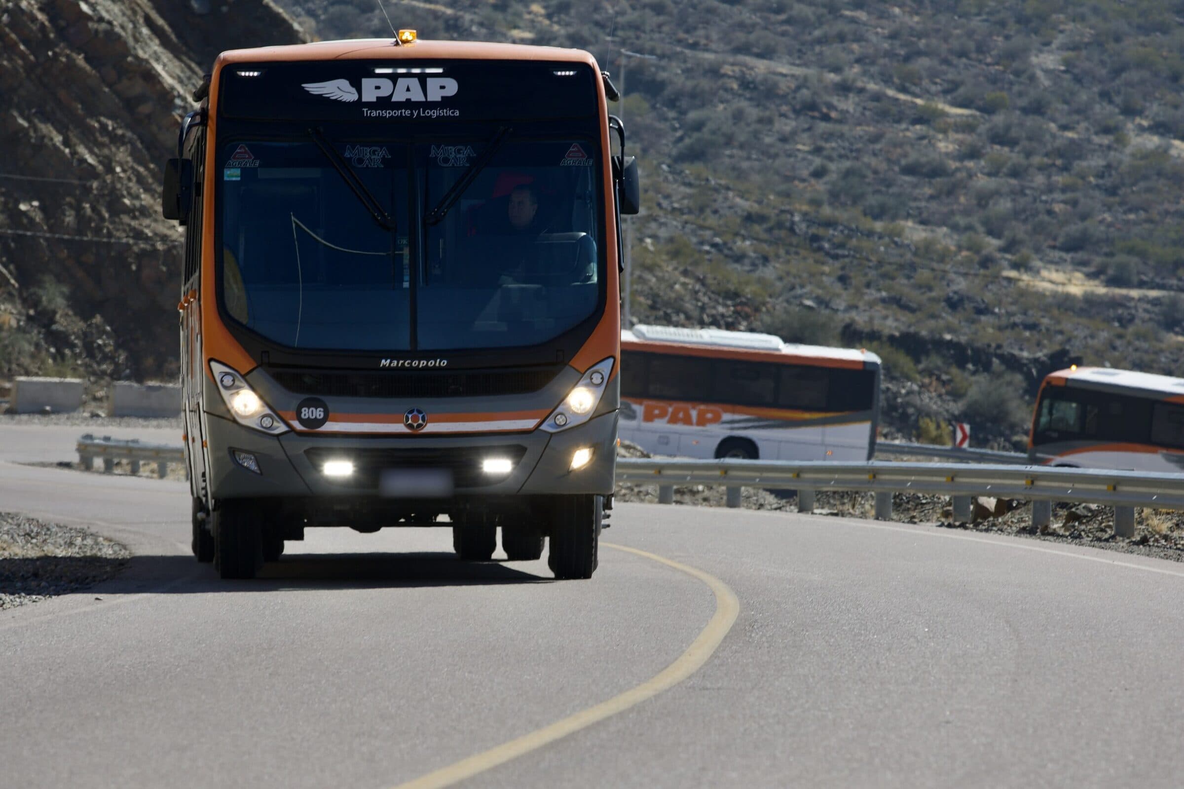 Bus PAP Transporte y Logística de frente en una curva de montaña, seguido por otras dos unidades